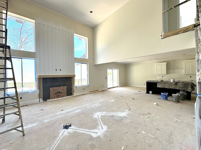 unfurnished living room with baseboards, a wealth of natural light, and a towering ceiling