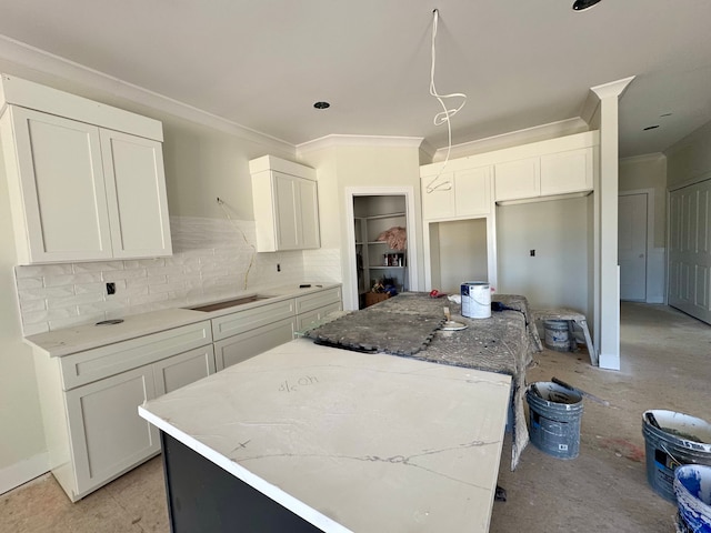 kitchen featuring white cabinets, a center island, tasteful backsplash, ornamental molding, and stovetop