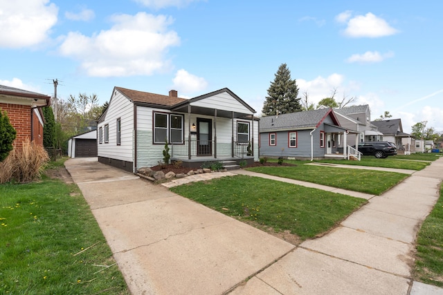 bungalow-style house featuring a detached garage, a porch, a front yard, an outbuilding, and a chimney