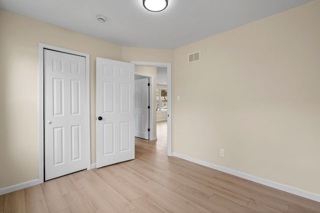unfurnished bedroom with baseboards, light wood-style flooring, visible vents, and a closet