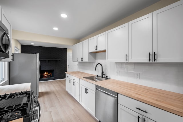 kitchen featuring a sink, black appliances, butcher block countertops, and a brick fireplace