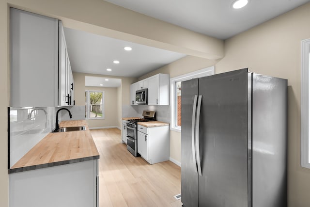 kitchen with butcher block countertops, a sink, appliances with stainless steel finishes, and tasteful backsplash