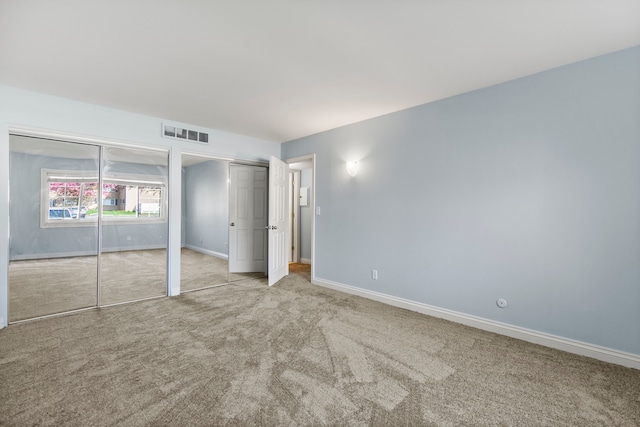 unfurnished bedroom with two closets, baseboards, visible vents, and carpet