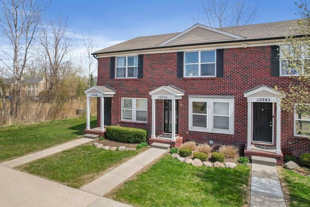 townhome / multi-family property featuring a shingled roof, a front lawn, and brick siding