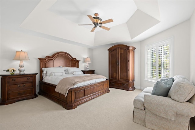 bedroom with a ceiling fan, a tray ceiling, and light colored carpet