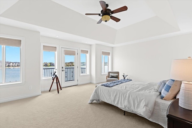 bedroom featuring a water view, a tray ceiling, light carpet, baseboards, and access to outside