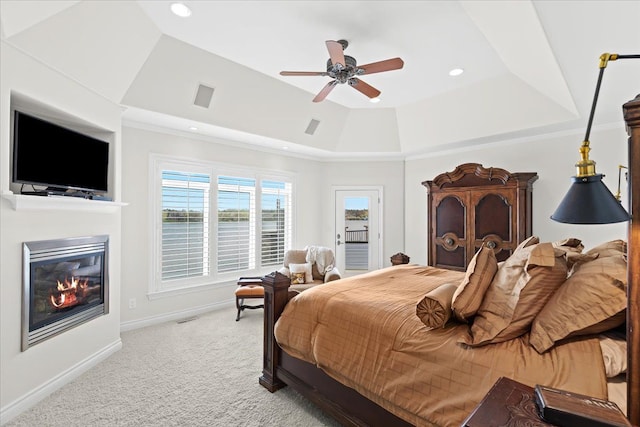 bedroom featuring a tray ceiling, baseboards, a glass covered fireplace, access to outside, and light colored carpet
