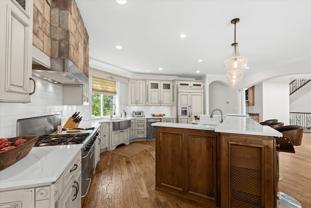 kitchen with a sink, light wood finished floors, backsplash, arched walkways, and appliances with stainless steel finishes