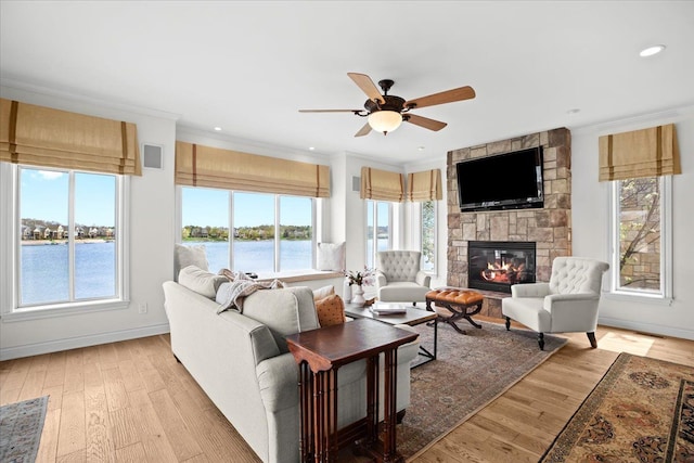 living room with ceiling fan, a stone fireplace, light wood-style flooring, and ornamental molding