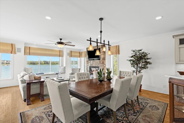 dining space with light wood-type flooring, crown molding, a stone fireplace, and recessed lighting
