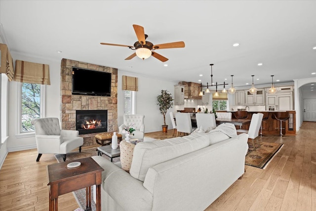 living room with a ceiling fan, a wealth of natural light, a stone fireplace, and light wood finished floors