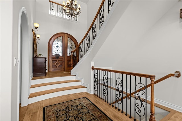foyer featuring an inviting chandelier, stairs, a towering ceiling, wood finished floors, and arched walkways