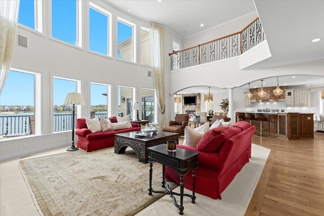 living area featuring light wood finished floors, visible vents, a towering ceiling, and a healthy amount of sunlight