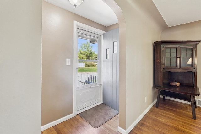 doorway to outside with baseboards, arched walkways, and light wood-style flooring
