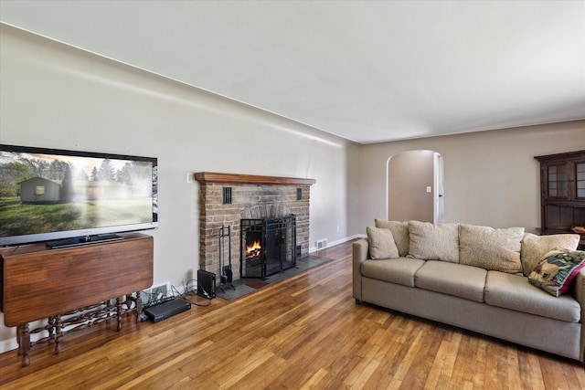 living area featuring arched walkways, wood-type flooring, a brick fireplace, and visible vents