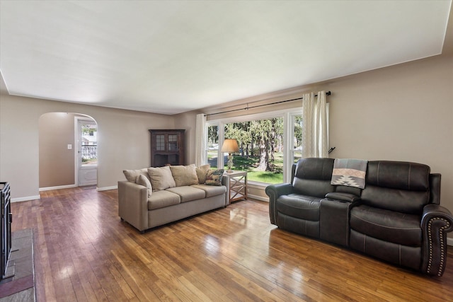 living room featuring arched walkways, baseboards, and hardwood / wood-style floors