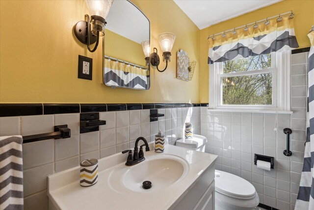 full bathroom with toilet, tile walls, a wainscoted wall, and vanity
