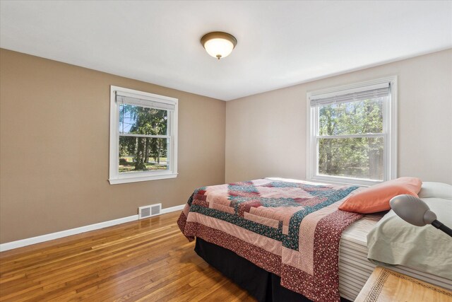 bedroom featuring baseboards, multiple windows, wood finished floors, and visible vents