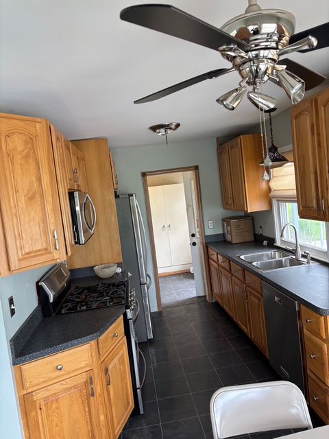 kitchen with a sink, dark countertops, dark tile patterned flooring, a ceiling fan, and stainless steel appliances
