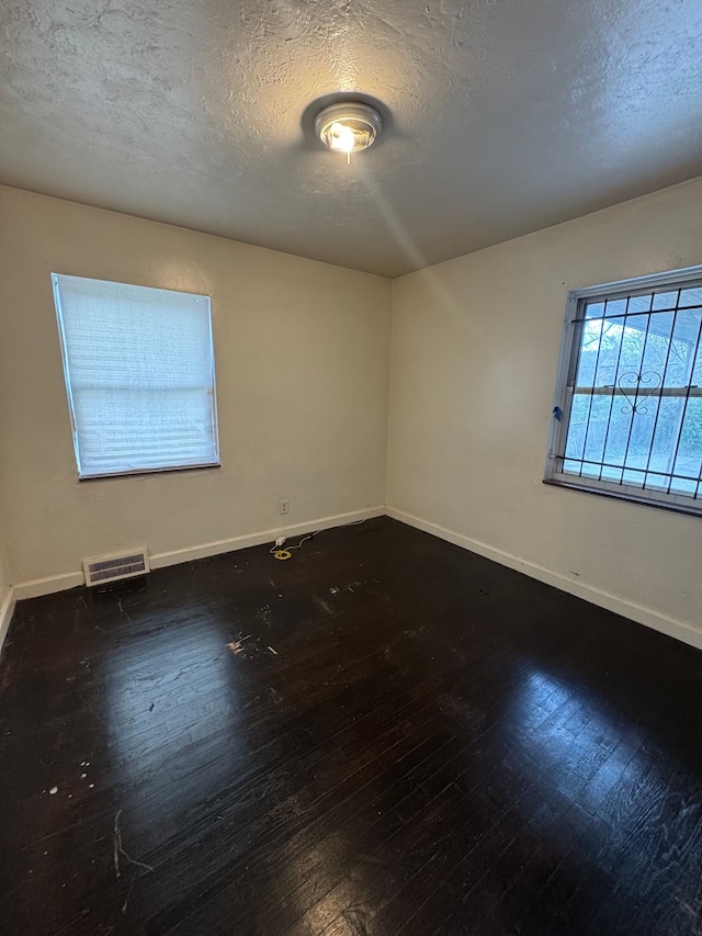 empty room with baseboards, a textured ceiling, hardwood / wood-style floors, and visible vents