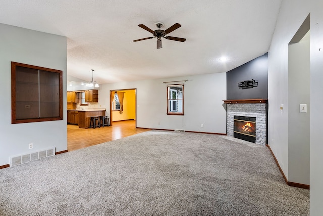 unfurnished living room with a ceiling fan, a fireplace, visible vents, baseboards, and light colored carpet