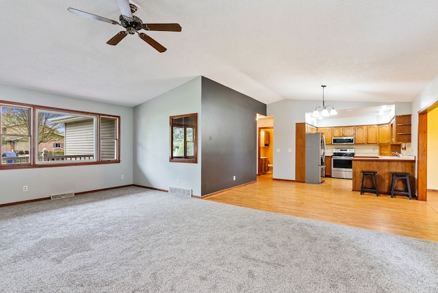 unfurnished living room with lofted ceiling, light carpet, a healthy amount of sunlight, and visible vents