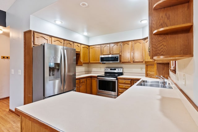kitchen with stainless steel appliances, a sink, a peninsula, open shelves, and light countertops