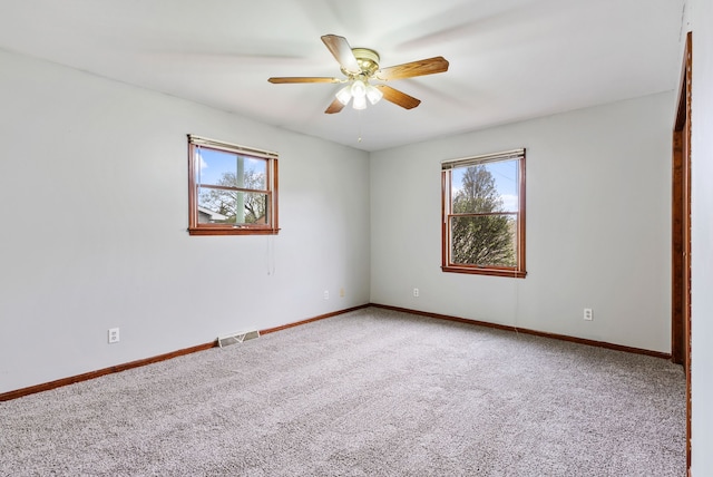 empty room with carpet flooring, baseboards, a ceiling fan, and visible vents