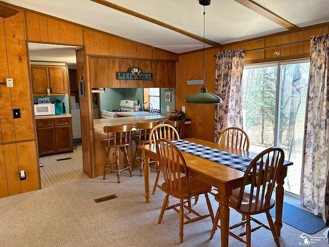 dining area featuring visible vents, light colored carpet, wood walls, lofted ceiling with beams, and washer / dryer