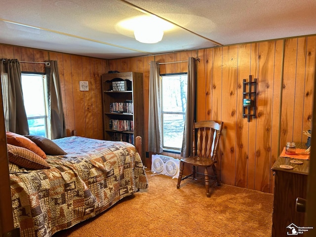 bedroom with carpet floors, a textured ceiling, wood walls, and multiple windows