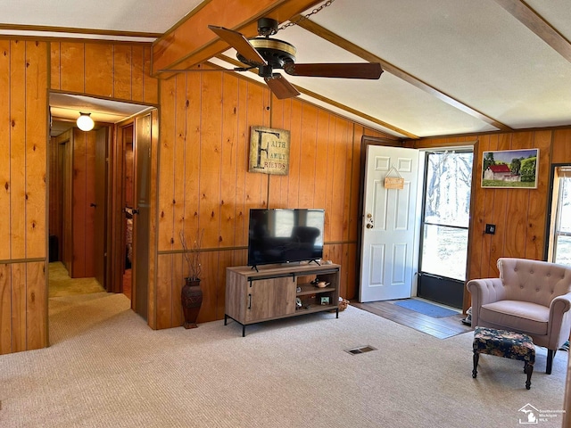 carpeted living room featuring lofted ceiling with beams, ceiling fan, and wooden walls
