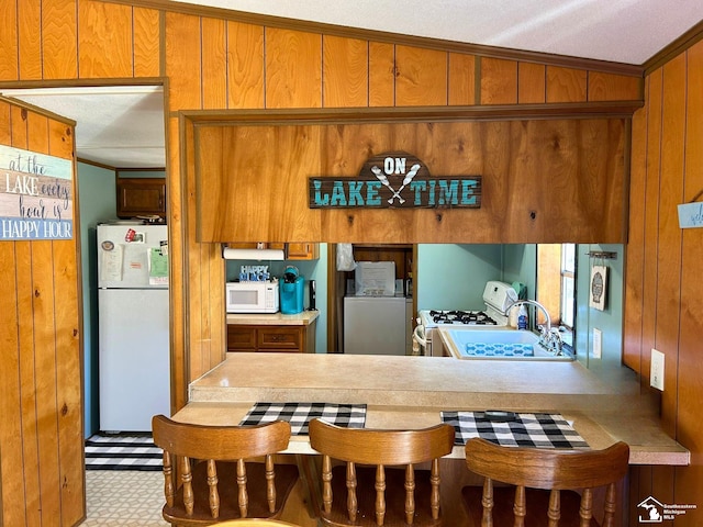 kitchen with brown cabinetry, a sink, washer / dryer, and white appliances