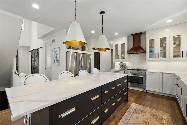 kitchen with wall chimney range hood, white cabinets, stainless steel appliances, backsplash, and a kitchen island