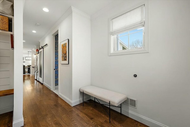 hallway with visible vents, a barn door, wood finished floors, and ornamental molding