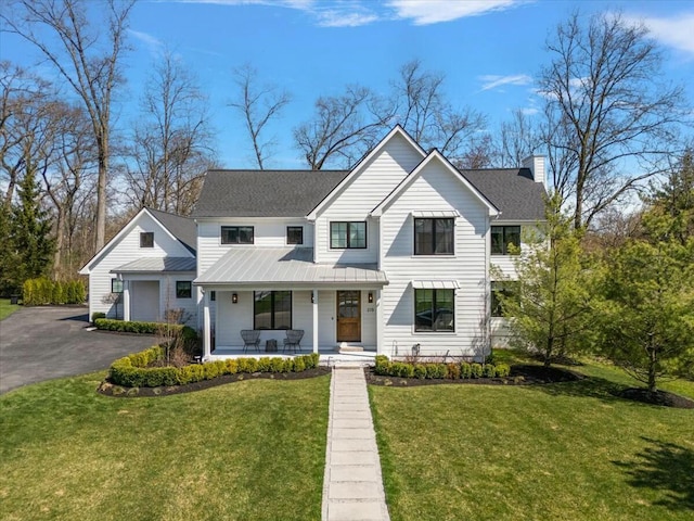 view of front of property with a front yard, a chimney, a standing seam roof, covered porch, and metal roof