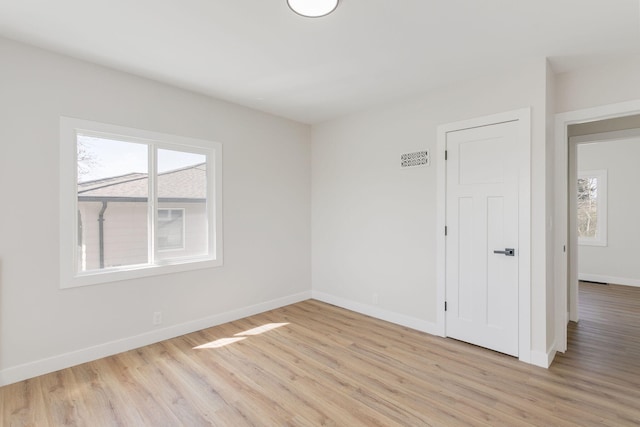 spare room featuring plenty of natural light, light wood-style floors, and baseboards