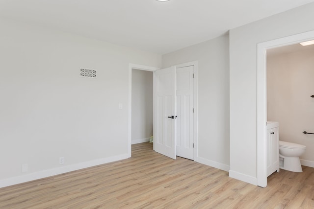 unfurnished bedroom featuring baseboards, visible vents, ensuite bathroom, and light wood-type flooring
