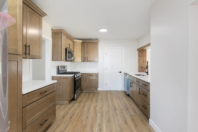kitchen with a sink, light wood finished floors, light countertops, stainless steel appliances, and baseboards