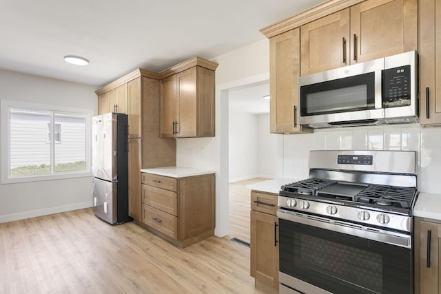 kitchen featuring light wood-type flooring, light countertops, appliances with stainless steel finishes, and tasteful backsplash