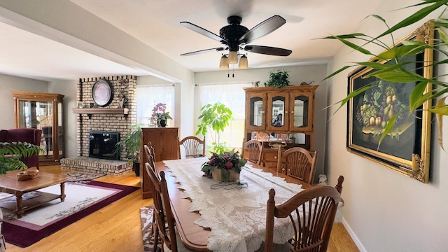 dining space with light wood-style floors, baseboards, a fireplace, and a ceiling fan