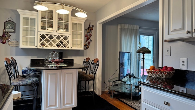 kitchen with white cabinetry, a breakfast bar area, dark countertops, and glass insert cabinets