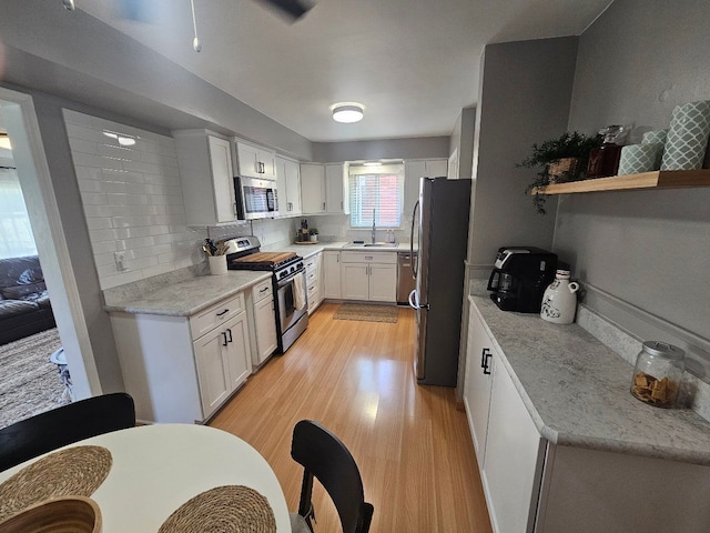 kitchen featuring light wood-type flooring, white cabinets, light stone counters, a sink, and appliances with stainless steel finishes