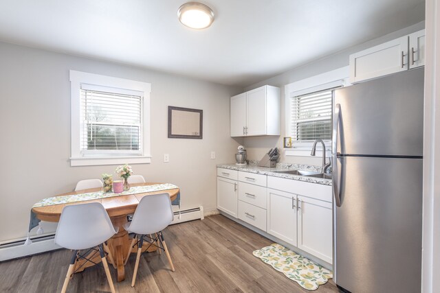 kitchen featuring freestanding refrigerator, wood finished floors, baseboard heating, white cabinetry, and a sink