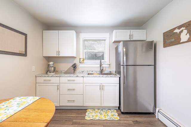 kitchen with white cabinets, light stone countertops, baseboard heating, freestanding refrigerator, and wood finished floors