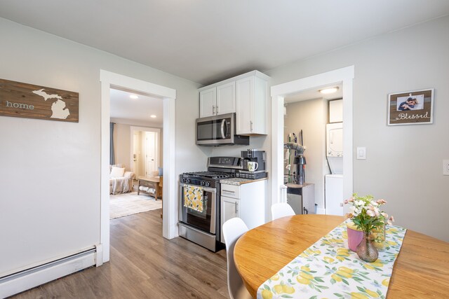 kitchen featuring stacked washer / dryer, dark wood finished floors, a baseboard radiator, stainless steel appliances, and white cabinetry