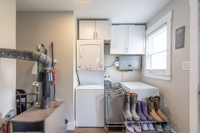 laundry area featuring stacked washer and clothes dryer, cabinet space, and wood finished floors
