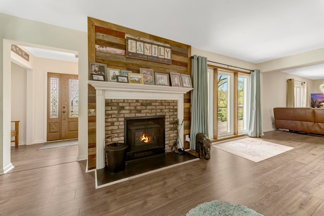 living area with baseboards, a brick fireplace, and wood finished floors