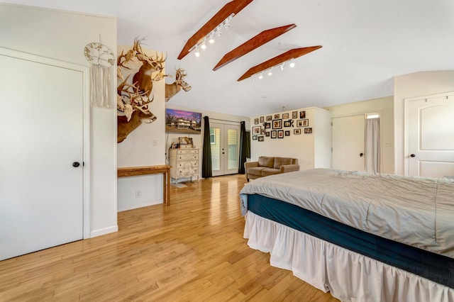 bedroom with french doors, track lighting, lofted ceiling with skylight, light wood-style floors, and access to outside