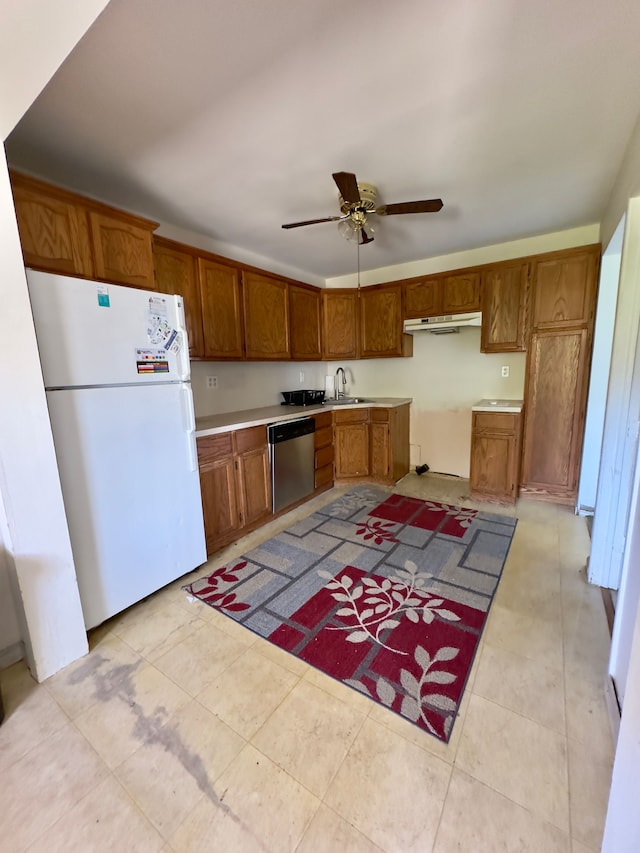 kitchen featuring a sink, brown cabinetry, freestanding refrigerator, stainless steel dishwasher, and under cabinet range hood