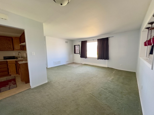 unfurnished living room with visible vents, a sink, baseboards, and light carpet